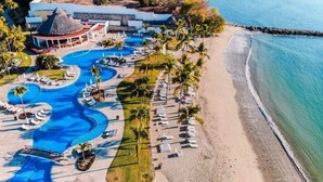 Vue aérienne d’un complexe hôtelier doté de plusieurs piscines, d’une plage et d’un bâtiment surmonté d’un toit de chaume.