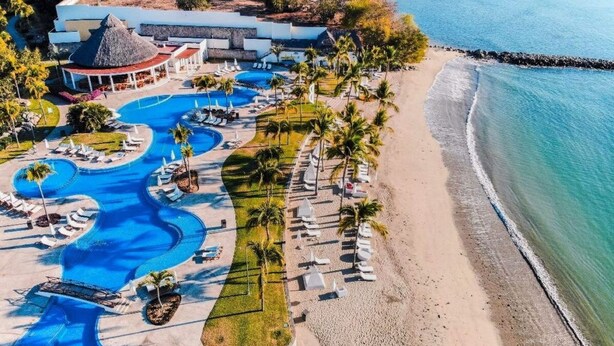 Vista aérea de un resort con varias piscinas, una playa y un edificio de techo de paja.