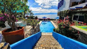 Zona de piscina con vista al mar, rodeada de plantas en macetas y mobiliario de exterior.