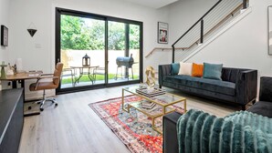 A modern living room with a sofa, coffee table, and a desk with a chair. There is a large sliding glass door leading to an outdoor area with a barbecue grill. - Modern 3BD/2.5 B in The heart Houston minutes from Downtown /Heights (Houston)