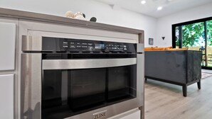 A modern kitchen with a built-in oven and microwave, a grey sofa, and a large window offering a view of greenery outside. - Modern 3BD/2.5 B in The heart Houston minutes from Downtown /Heights (Houston)