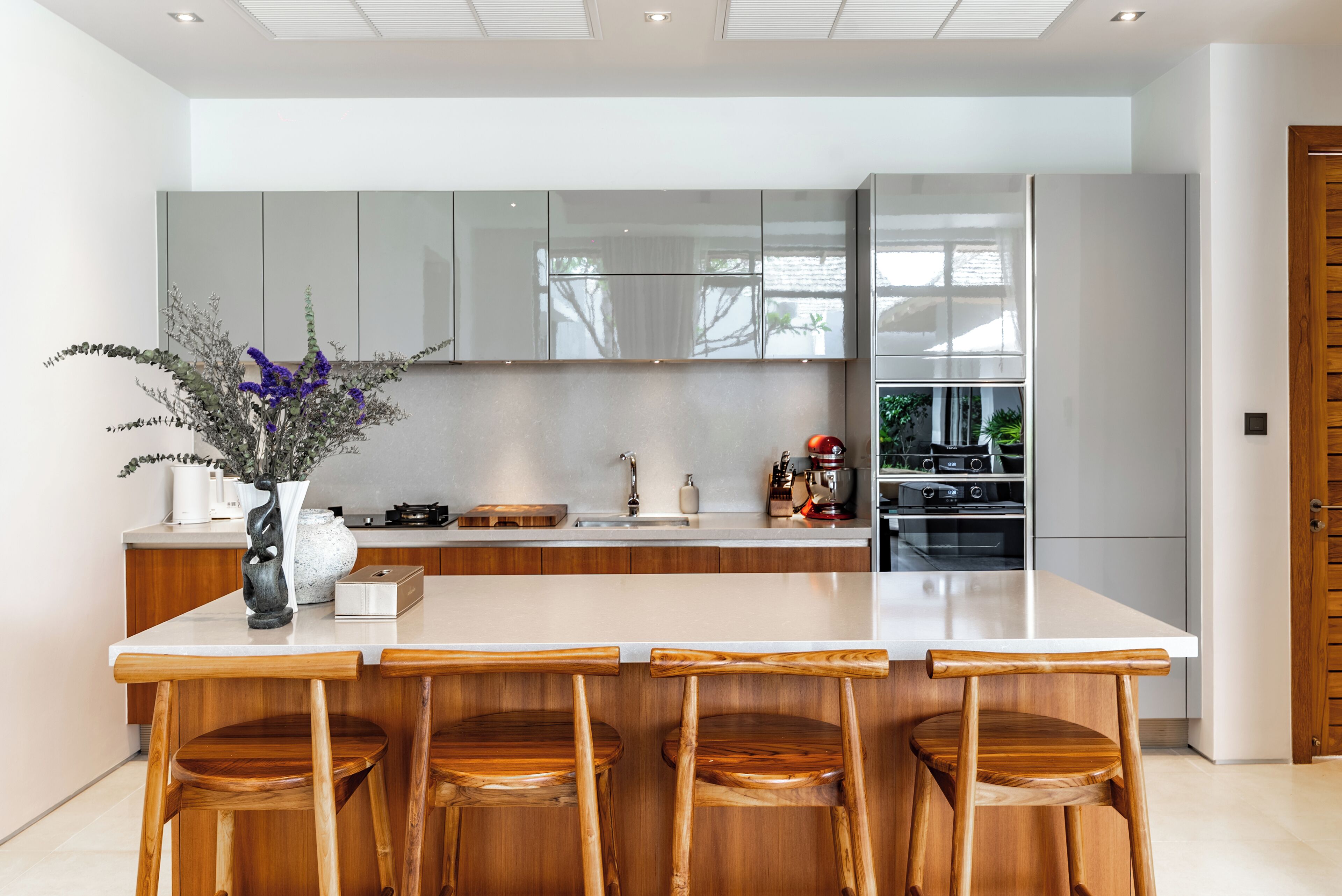 A modern kitchen with a central island, wooden bar stools, and a vase with flowers.