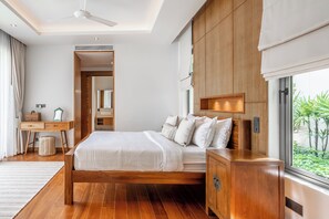 A modern bedroom with a wooden bed, bedside tables, a desk, and a large window with a view of greenery. - Anchan Flora By Villacarte (Thep Krasattri)