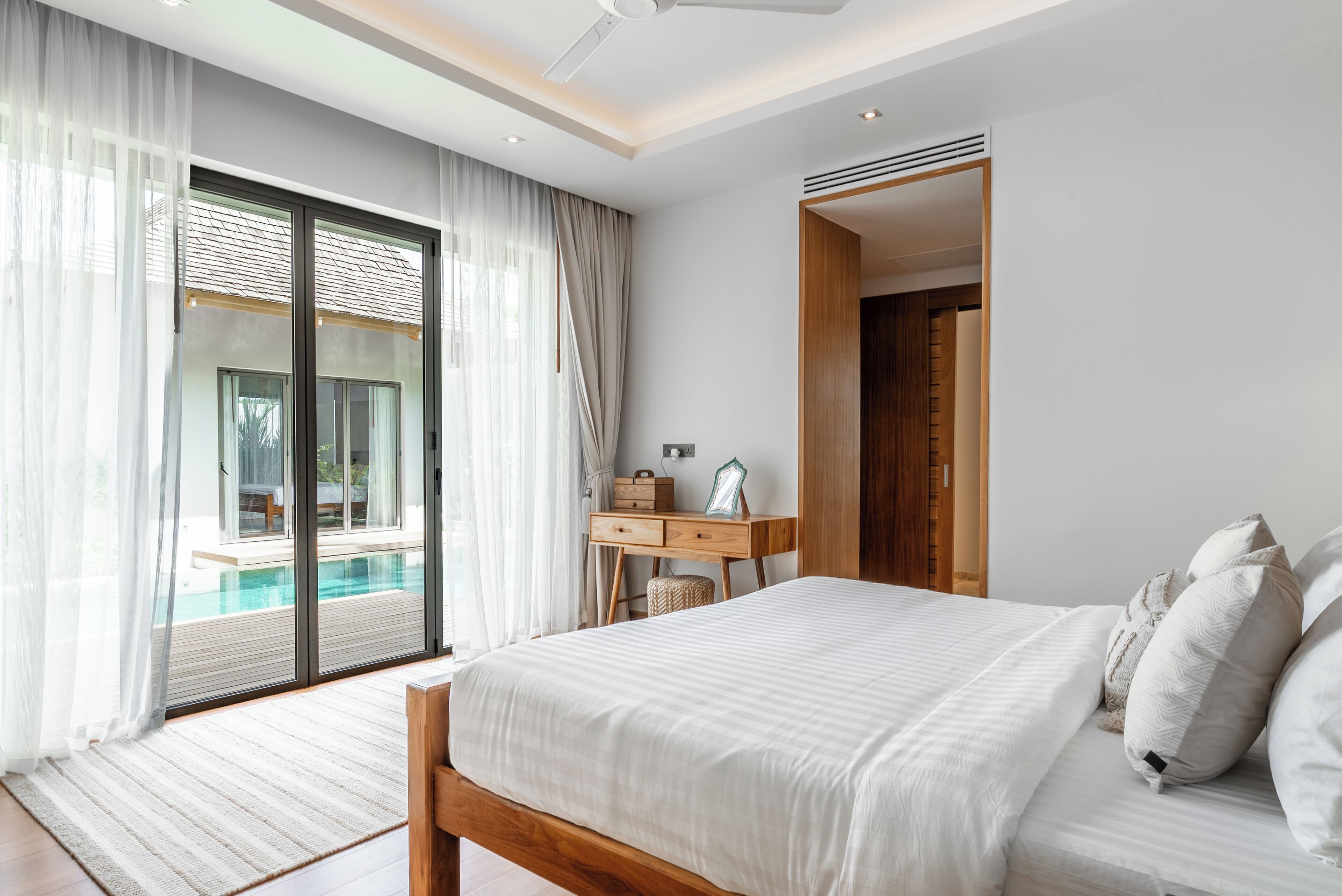 A bedroom with a large bed, a desk, and a view of a swimming pool.