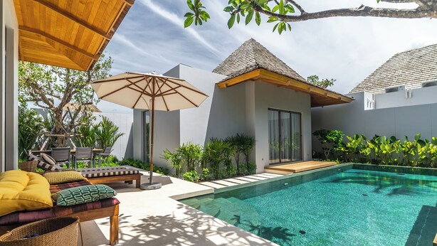 A modern outdoor pool area with a lounge chair, umbrella, and a small building with a tiled roof. - Anchan Flora By Villacarte (Thep Krasattri)