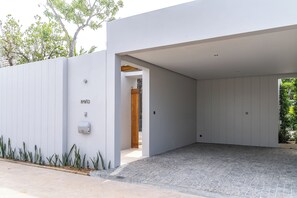 A modern building with a clean, white exterior, a paved entrance area, and a visible door leading to the interior. - Anchan Flora By Villacarte (Thep Krasattri)