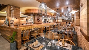 Un restaurante con paneles de madera, mesas de mármol, sillas de mimbre e iluminación colgante distintiva.