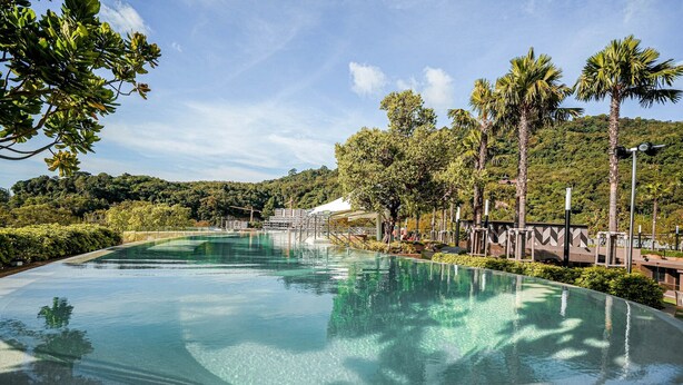 Una piscina amplia y cristalina rodeada de palmeras y vegetación, con vistas a un paisaje montañoso al fondo.