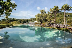 A large, clear swimming pool surrounded by palm trees and greenery, with a view of a hilly landscape in the background. - Apartament Mari By Villacarte (Kamala)
