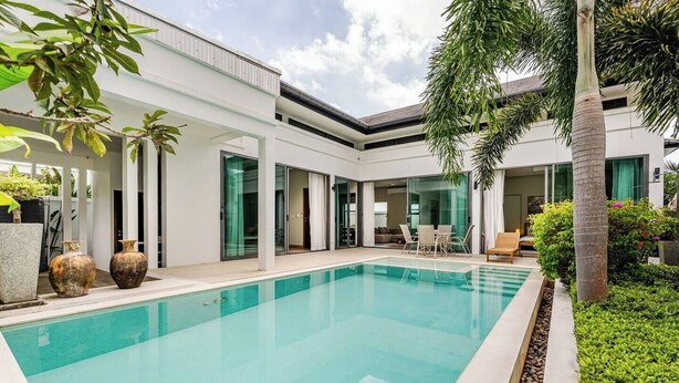 Un área de piscina moderna con una pileta cristalina, rodeada por un edificio blanco con puertas de vidrio y un patio cubierto.