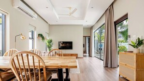 Un comedor moderno con una mesa y sillas de madera, un televisor de pantalla plana y vistas al exterior a través de grandes ventanales.
