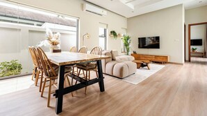 Una sala de estar moderna con comedor, que incluye una mesa de comedor de madera, asientos cómodos, un sofá, un televisor y un ventanal grande.