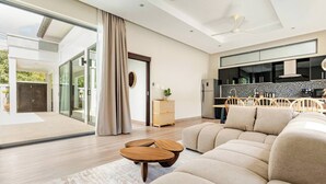 Una sala de estar moderna con un sofá seccional grande, una mesa de centro de madera y un comedor con una cocina al fondo.