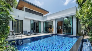 Une maison moderne dotée d’une piscine, de grandes portes vitrées et de mobilier d’extérieur.