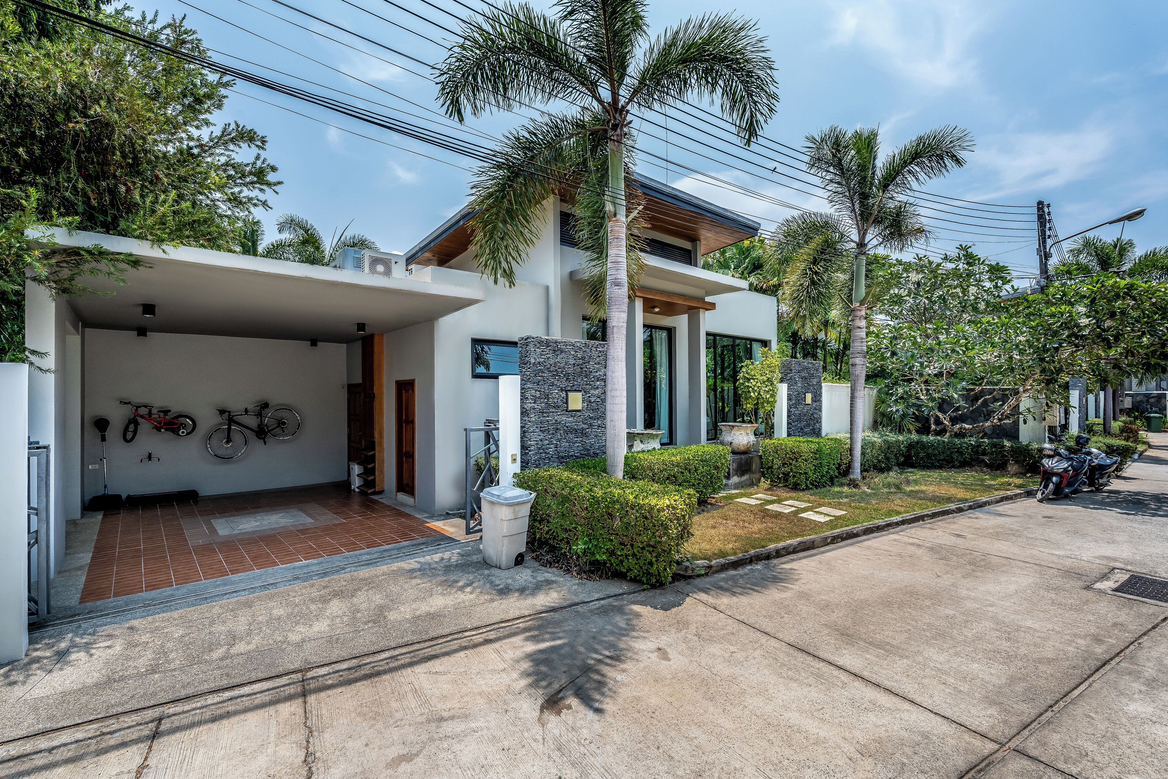 A modern house with a garage, a covered entrance, and a well-maintained garden with palm trees and shrubs.