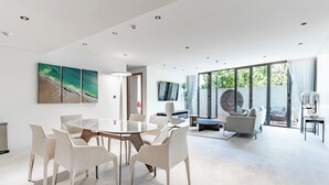Ein großzügiges, modernes Wohnzimmer mit einem runden Esstisch, weißen Stühlen, einer Couch und einem an der Wand befestigten Fernseher.
