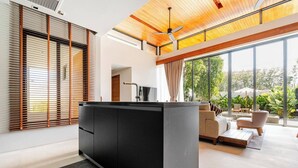 Una sala de estar moderna con mueble de entretenimiento negro, ventilador de techo, ventanas amplias y vistas al exterior.