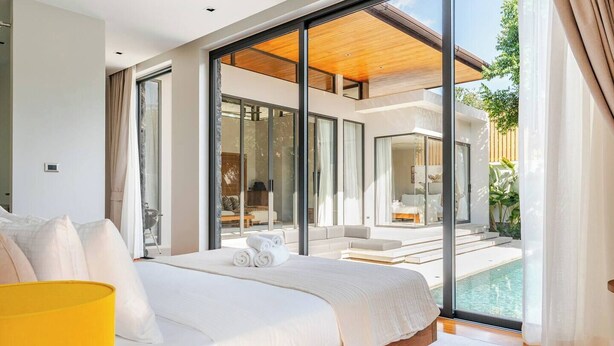 Un dormitorio moderno con una cama grande, vista a una piscina y una puerta de vidrio que da a un área de estar.