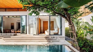 Una casa moderna con piscina, puertas de cristal que dan a un salón y una terraza de madera.