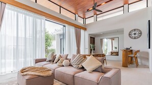 Amplia sala de estar con un sofá modular grande, techo de madera y un comedor con mesa y sillas de madera.