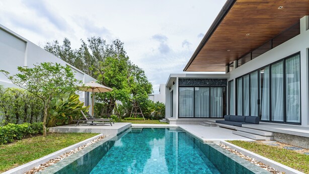 Una casa moderna con piscina, rodeada de vegetación y una terraza de madera.