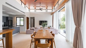 Un comedor amplio con una mesa y sillas de madera, una cocina al fondo y ventanas grandes con cortinas.