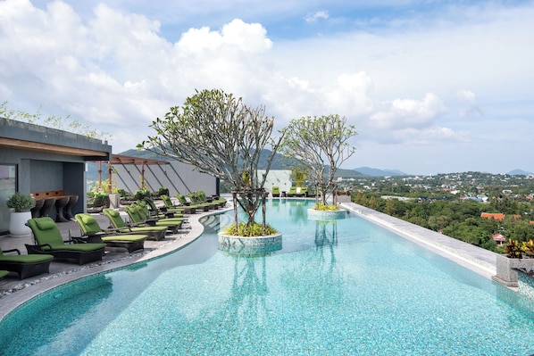 A pool with lounge chairs and planters, surrounded by a building with a view of distant mountains.