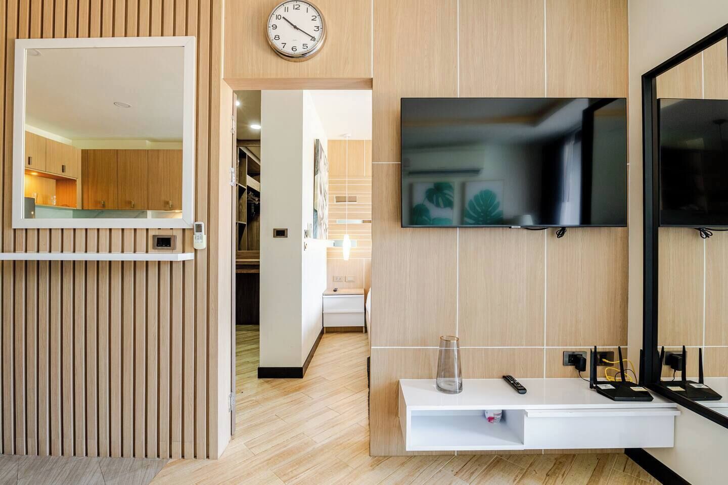 A modern living room with a wooden panel wall, a mounted TV, a clock, and a minimalist console table.