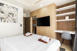 A hotel room with a bed, a TV mounted on the wall, a wooden panel wall, and a small desk with a chair.