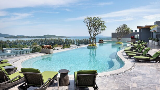 Un espace piscine avec des chaises longues, un petit îlot et une vue sur la mer et les collines.
