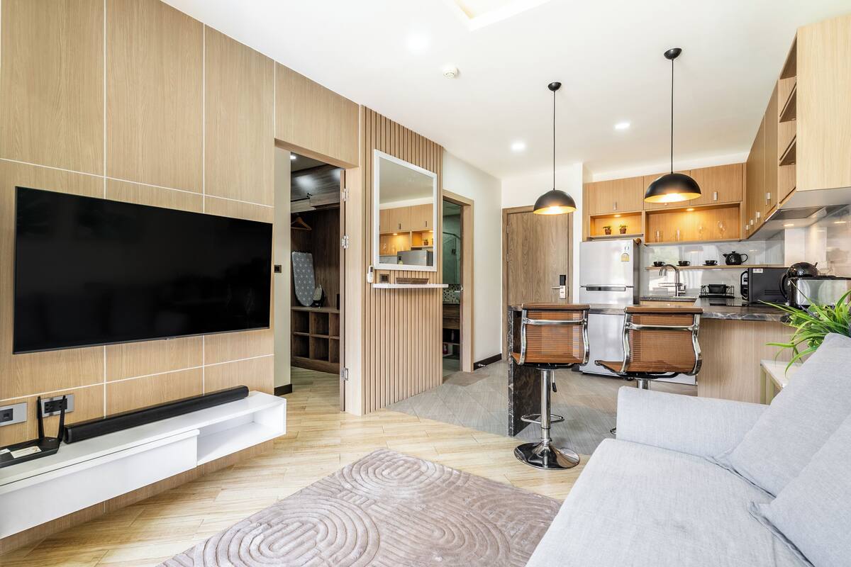 A modern kitchen with wooden cabinets, a built-in TV, and a bar area.
