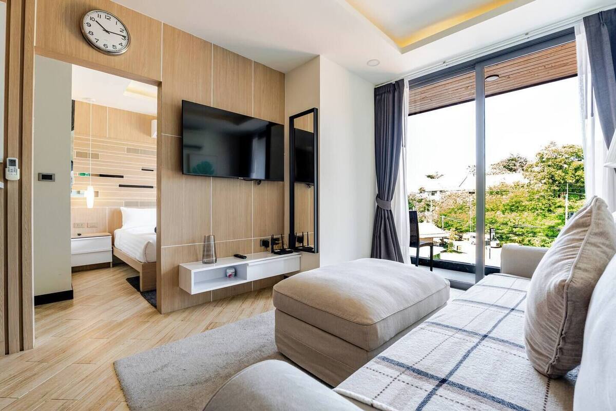 A modern hotel room with a bed, a TV, a sofa, and a balcony with a view.