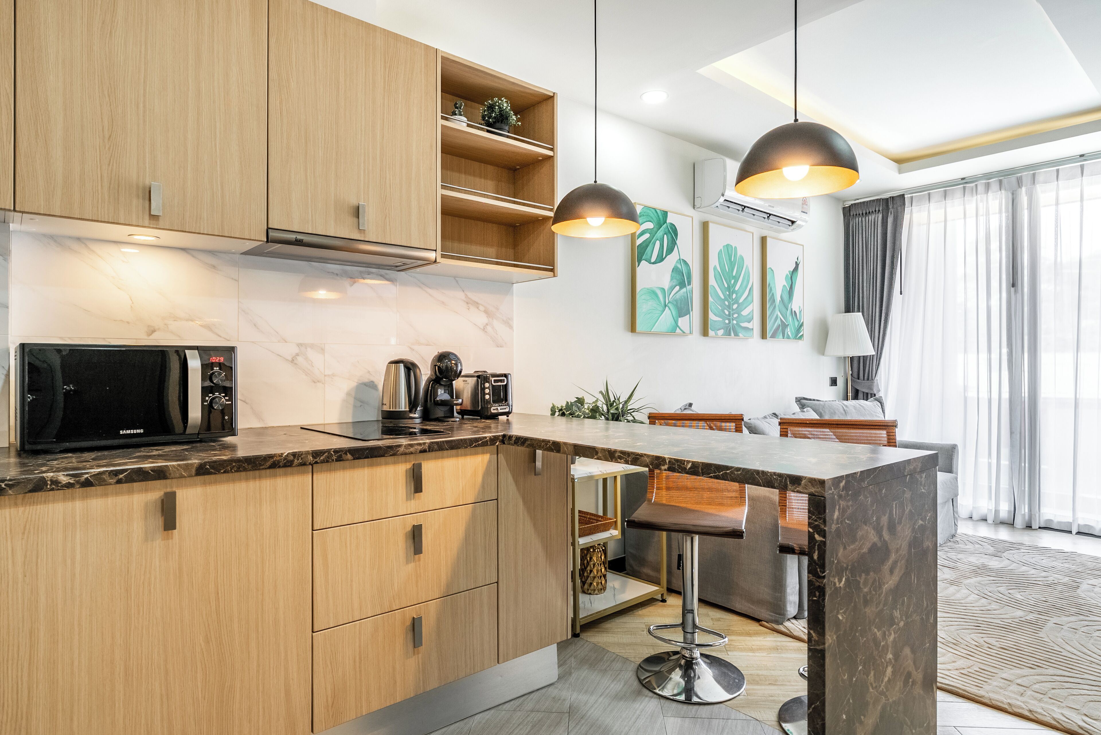 Una cocina moderna con armarios de madera, encimera de mármol, microondas integrado, cafetera y un taburete de bar.