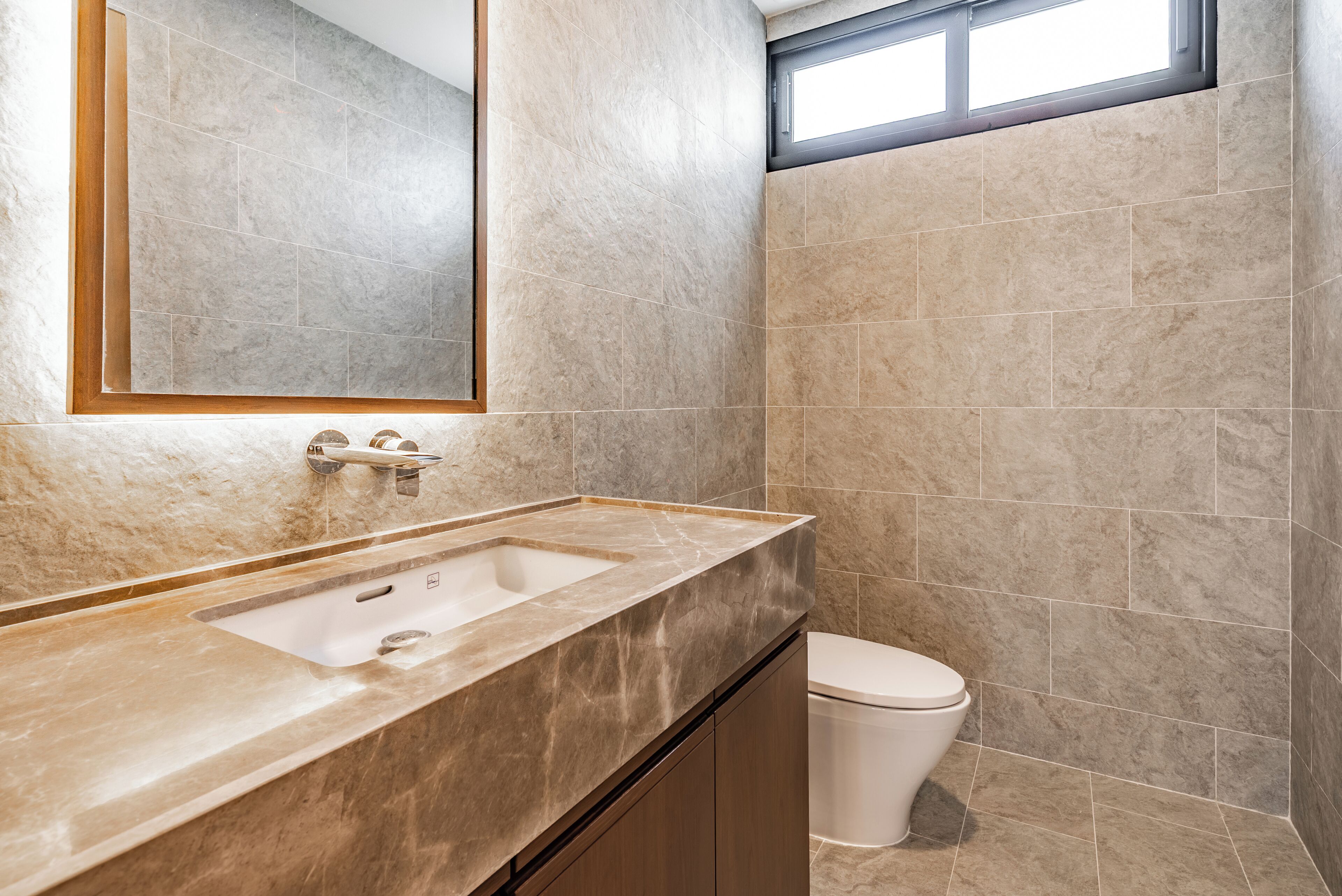 A bathroom with a marble sink, a toilet, and a large mirror.