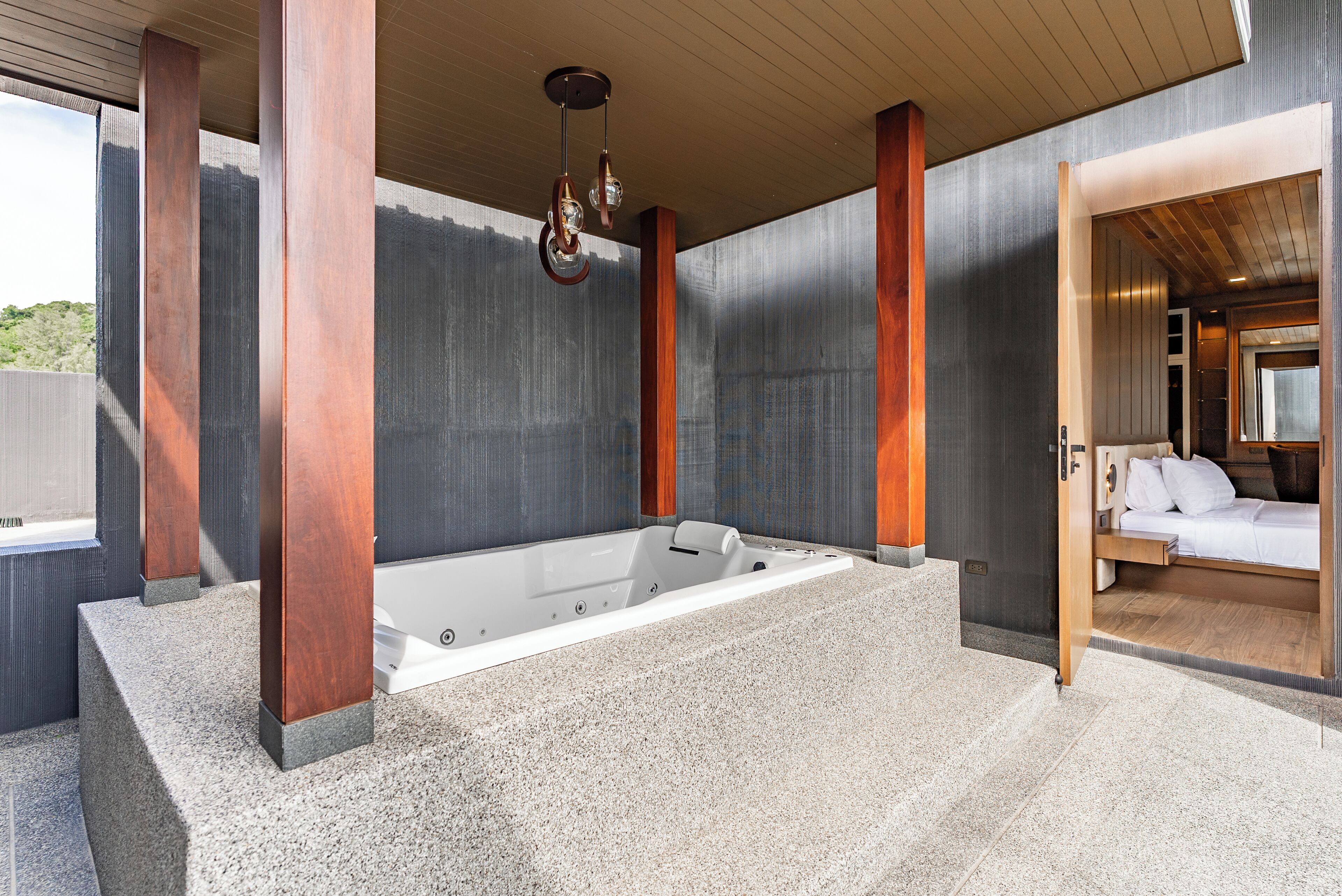 Et moderne spa-område med et stort badekar, træsøjler og et lille opholdsområde ved siden af.
