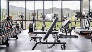Un gimnasio moderno con diversos equipos de ejercicio, amplias ventanas que ofrecen vistas a colinas y un interior limpio y espacioso.