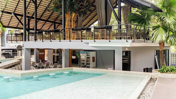 Zona de piscina con área de descanso cubierta, bar y bar en la piscina.