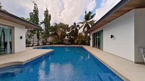 A swimming pool with a tiled deck, surrounded by palm trees and a modern building with large windows. - Mandala By Villacarte (Choeng Thale)