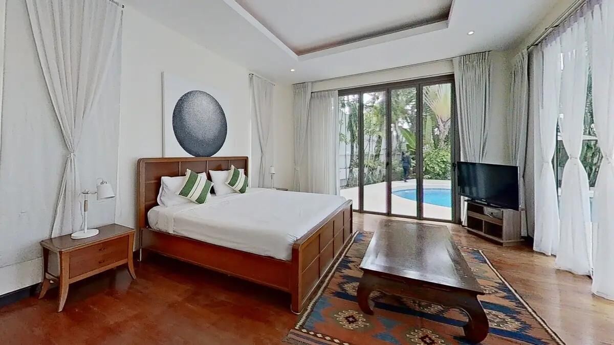 A bedroom with a bed, a TV, a nightstand, and a view of a swimming pool.