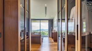A modern hotel room with a wooden floor, large sliding glass doors leading to a balcony with a city view. - La vista Villas by Villacarte (Chalong)