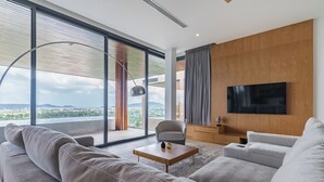 A modern living room with a large sofa, a coffee table, and a TV mounted on a wooden wall. - La vista Villas by Villacarte (Chalong)