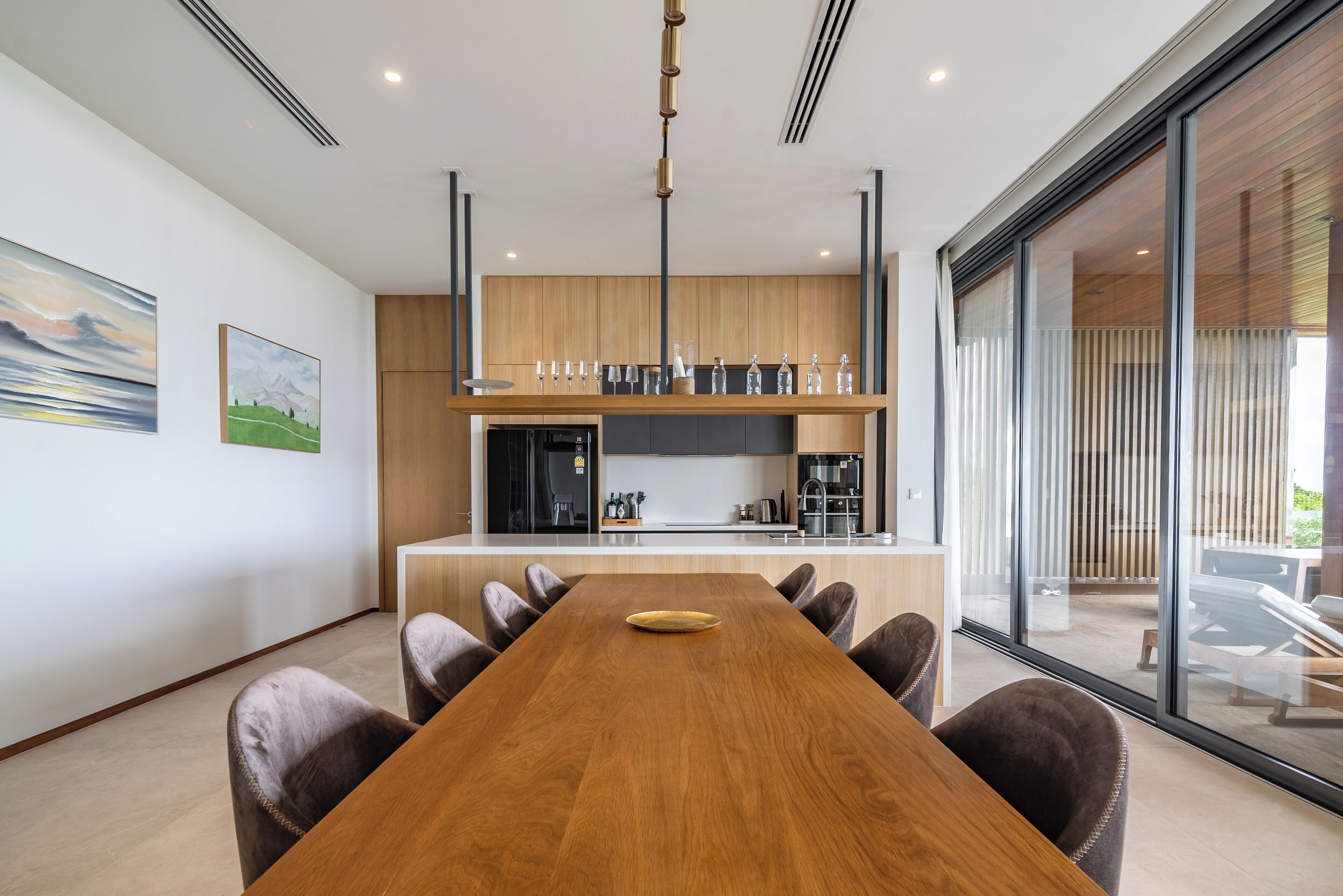 A modern kitchen with a central island, wooden cabinets, and a large dining table with chairs.