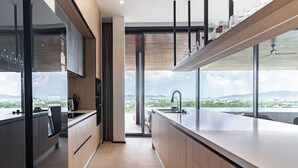A modern kitchen with a large island, a built-in oven, and a view of the city. - La vista Villas by Villacarte (Chalong)