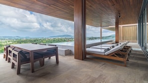 A modern outdoor dining area with a wooden table and chairs, a sofa with cushions, and a view of the landscape. - La vista Villas by Villacarte (Chalong)