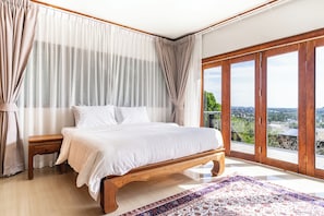 A bedroom with a large bed, a wooden nightstand, a view through a sliding glass door, and a patterned rug.