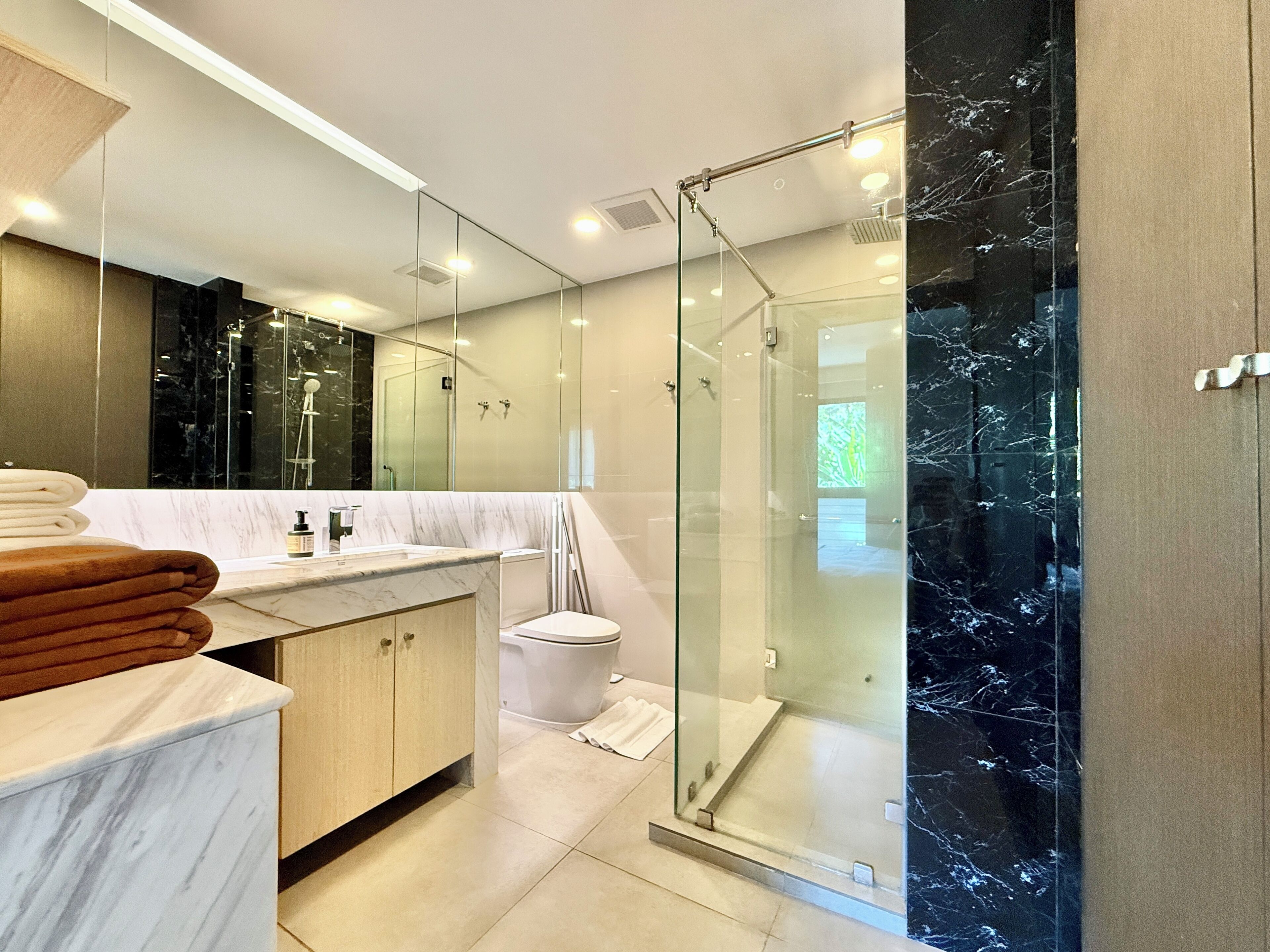 A modern bathroom with a glass-enclosed shower, a marble countertop, and a large mirror.