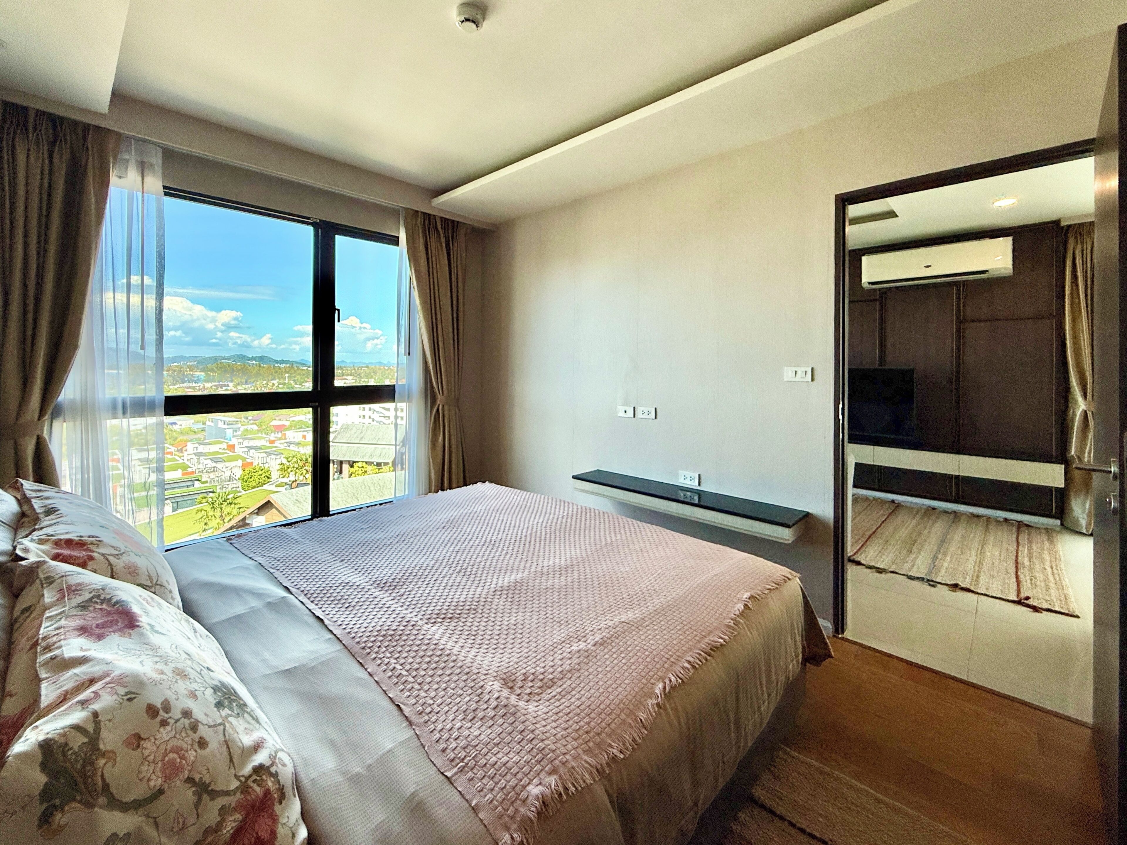 A bedroom with a large bed, a bedside table, a TV, and a view of the city.