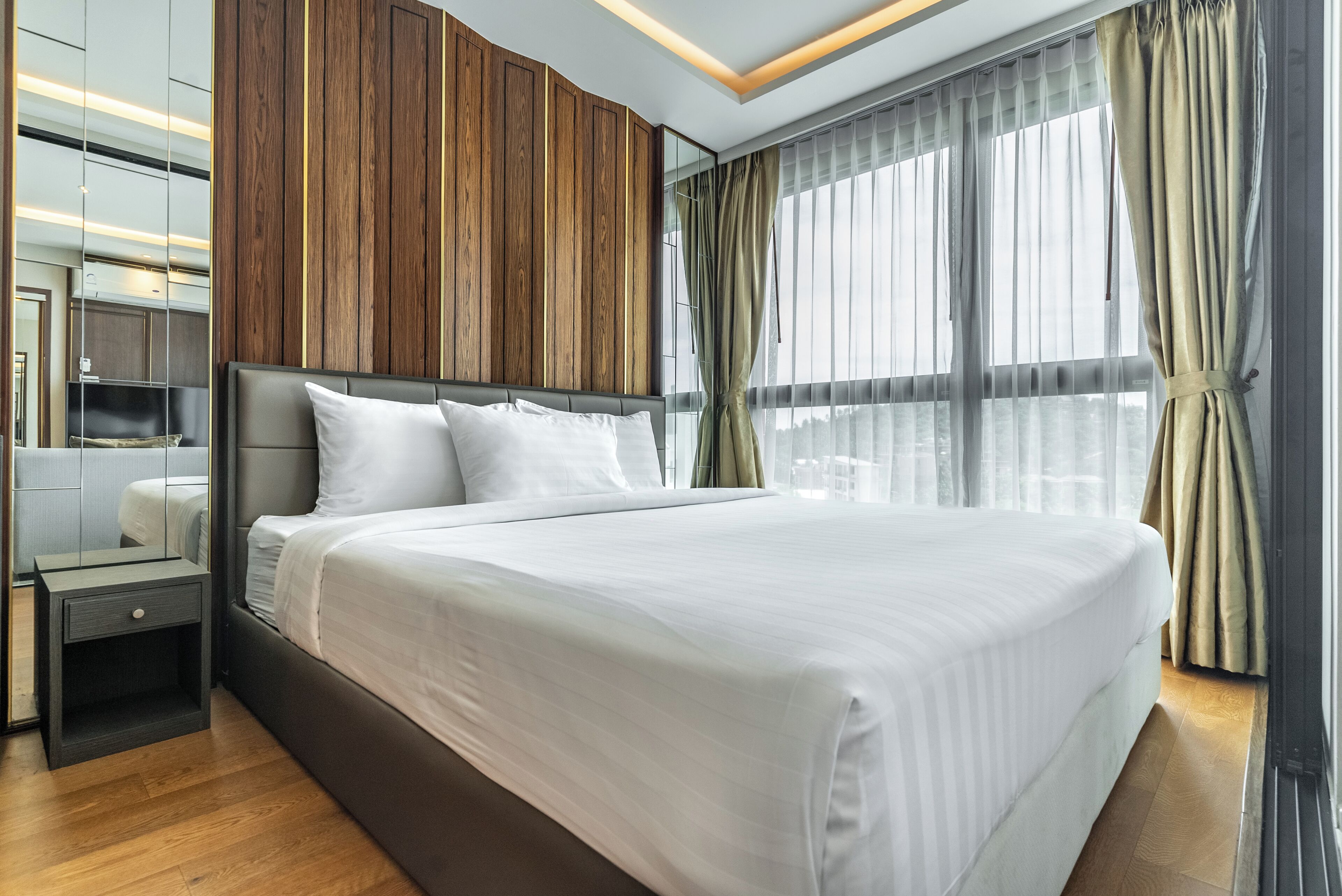Habitación de hotel moderna con una cama grande, panel de pared de madera y un amplio ventanal con cortinas.