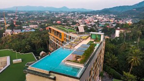 Een hotel met een dakterraszwembad, een groen dak en uitzicht op een stadsgezicht met bergen op de achtergrond.