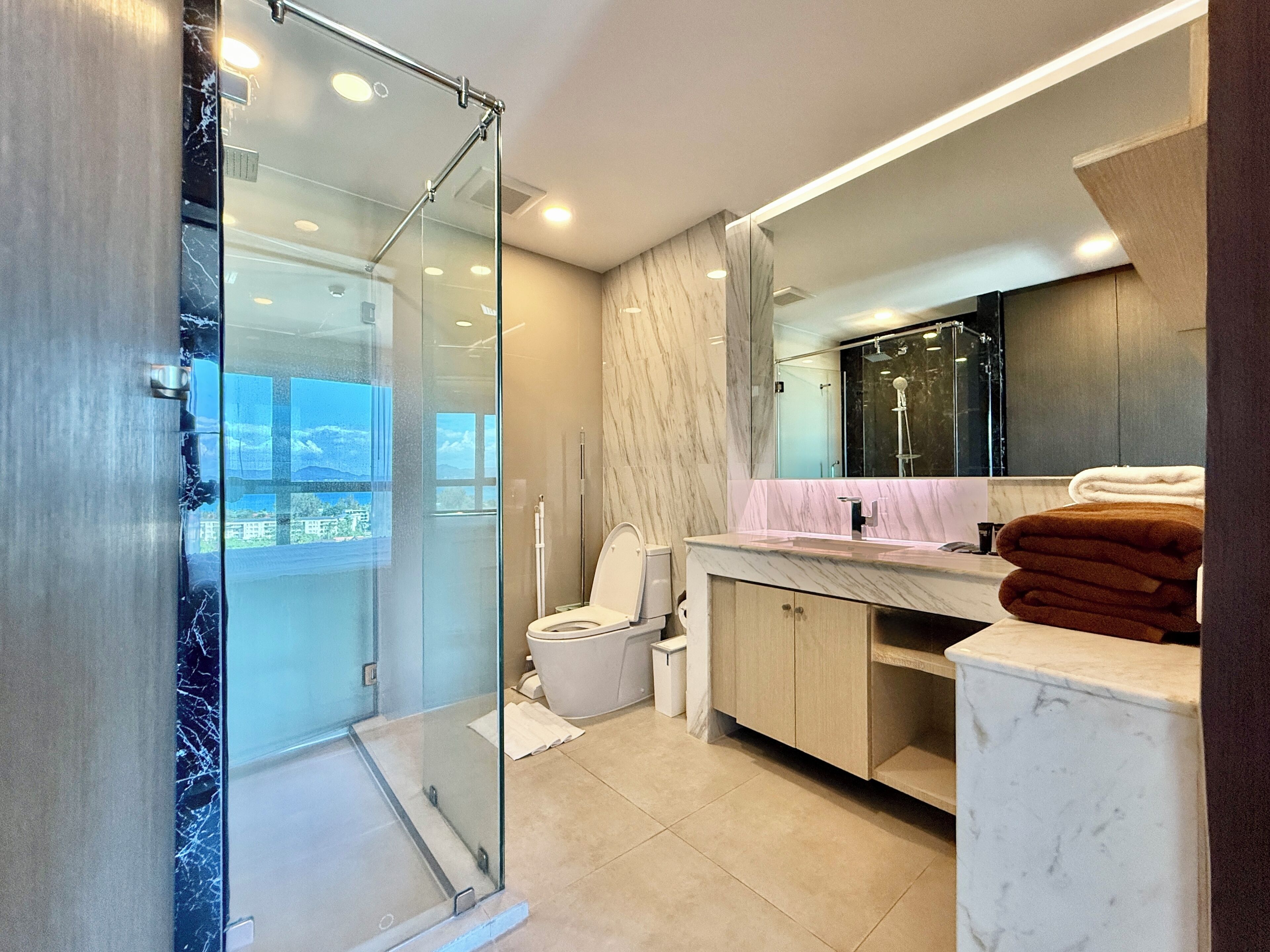 Ein modernes Badezimmer mit Duschkabine aus Glas, Toilette, Waschbecken mit Marmorplatte und großem Spiegel.